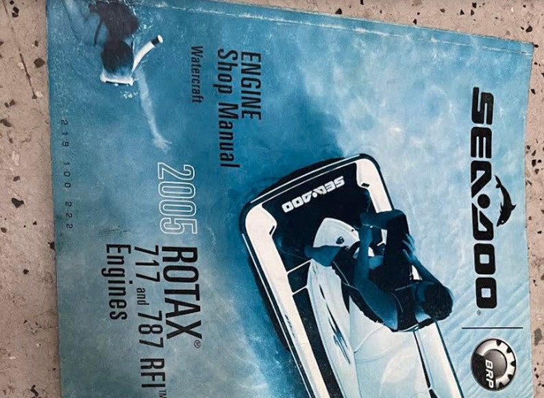 May include: A blue and white Sea-Doo shop manual for 2005 Rotax 717 and 787 RFI engines. The manual features a black and white illustration of a person riding a Sea-Doo jet ski.