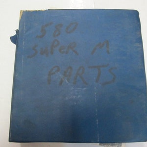 Puede incluir: Carpeta azul con el texto "580 Super M Parts" escrito en marcador negro.