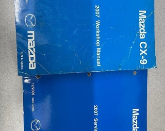 May include: Two blue Mazda CX-9 service manuals. The top manual is for the 2007 Workshop Manual and the bottom manual is for the 2007 Service Highlights. Both manuals have the Mazda logo and the date 12/2006.