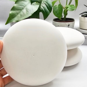 May include: Three white ceramic round discs stacked on top of each other. The discs are smooth and have a slightly glossy finish.
