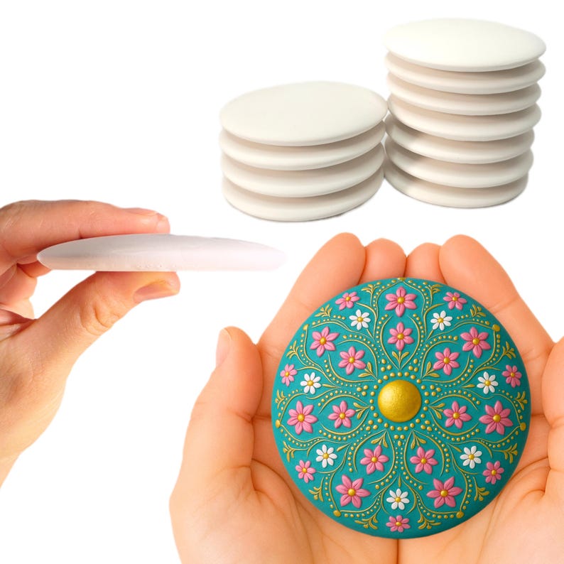 May include: A teal round ceramic tile with a floral design. The tile has pink and white flowers with gold accents. The tile is being held in a person's hands.