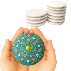May include: A teal blue round trinket box with a gold center and pink and white floral design. The box is being held in a person's hands.