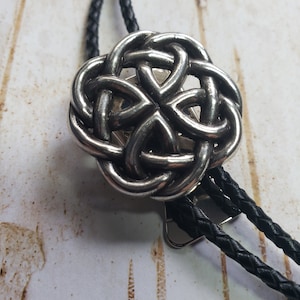 May include: A silver bolo tie with a Celtic knot design. The tie is made of braided black leather.