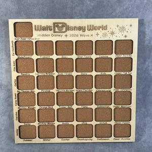 May include: A square wooden display board featuring a grid of thirty-six rectangular cork insets. The top is engraved with Walt Disney World Hidden Disney 2026 Wave A. Each row and column includes labels for specific character and theme collections.