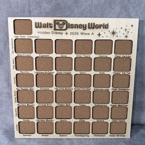 May include: Wooden display board with recessed squares for Disney pins. The board is engraved with "Walt Disney World Hidden Disney 2026 Wave A" and features various Disney character names and themes. The board is made of light-colored wood.