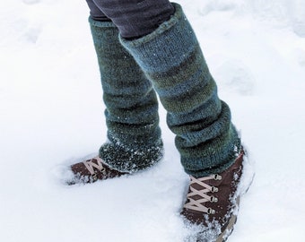 May include: A pair of green and blue striped leg warmers worn over black pants with brown hiking boots. The person is standing in the snow.