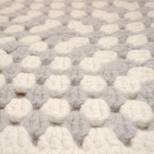 K&ouml;nnte beinhalten: Nahaufnahme einer wei&szlig;en und grauen Strickdecke mit einem strukturierten, bauschigen Design.