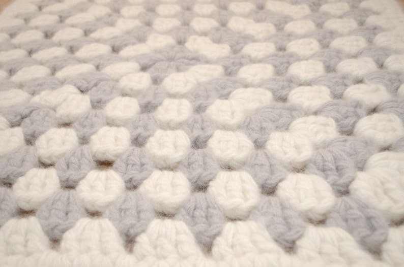 K&ouml;nnte beinhalten: Nahaufnahme einer wei&szlig;en und grauen Strickdecke mit einem strukturierten, bauschigen Design.