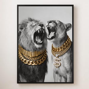Op de afbeelding: Zwart-wit ingelijste print met een leeuw en een leeuwin die brullen, beide versierd met gouden kettingen. De leeuw draagt een ketting in riemstijl, de leeuwin een dollarteken hanger. Het beeld heeft een modern, luxueus thema.