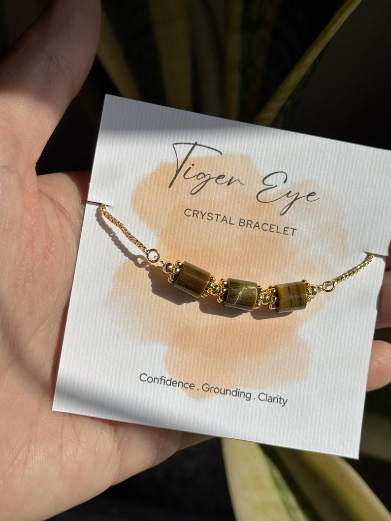 May include: A gold chain bracelet featuring tiger eye crystal beads. The bracelet is displayed on a card with the text "Tiger Eye Crystal Bracelet" and the words "Confidence, Grounding, Clarity."