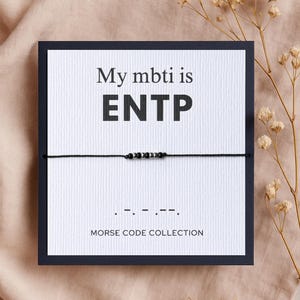 Op de afbeelding: Een witte kaart met zwarte tekst die "My mbti is ENTP" zegt en een zwart koordarmband met zwarte kralen. Het armband is in morsecode en de tekst onder het armband zegt "Morse Code Collection".