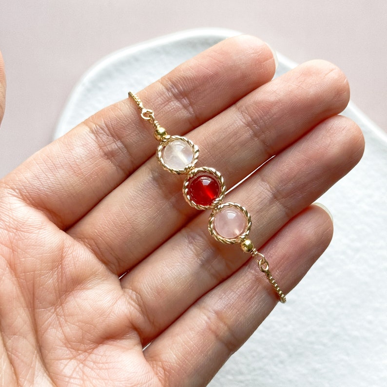 Peut inclure: Un bracelet dor&eacute; compos&eacute; de trois montures circulaires aux bords m&eacute;talliques torsad&eacute;s. La monture centrale contient une perle sph&eacute;rique rouge vif, tandis que les deux montures lat&eacute;rales renferment des perles sph&eacute;riques rose p&acirc;le translucides.