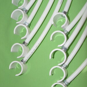 May include: White plastic pipe clamps with silver screws. The clamps are attached to white plastic pipes. The pipes are arranged in a fan shape on a green background.