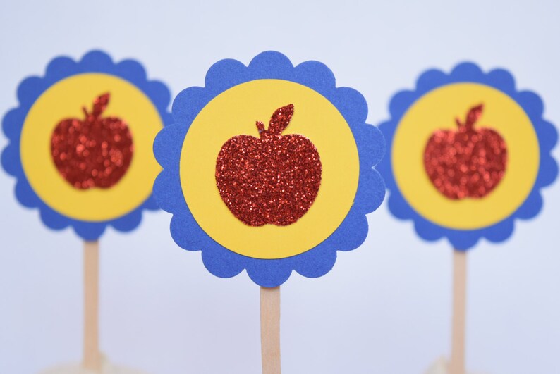 May include: Three red glitter apple cupcake toppers with yellow and blue scalloped circles. The toppers are on wooden sticks.