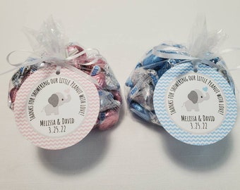 May include: Two small cellophane bags filled with Hershey's Kisses, one with pink and silver foil, the other with blue and silver foil. Each bag has a round tag with an elephant graphic and the text "Thanks for showering our little peanut with love!" and the names Melissa & David and the date 3.25.22.