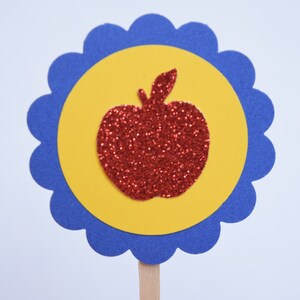 May include: A red glitter apple silhouette on a yellow circle with a blue scalloped border.