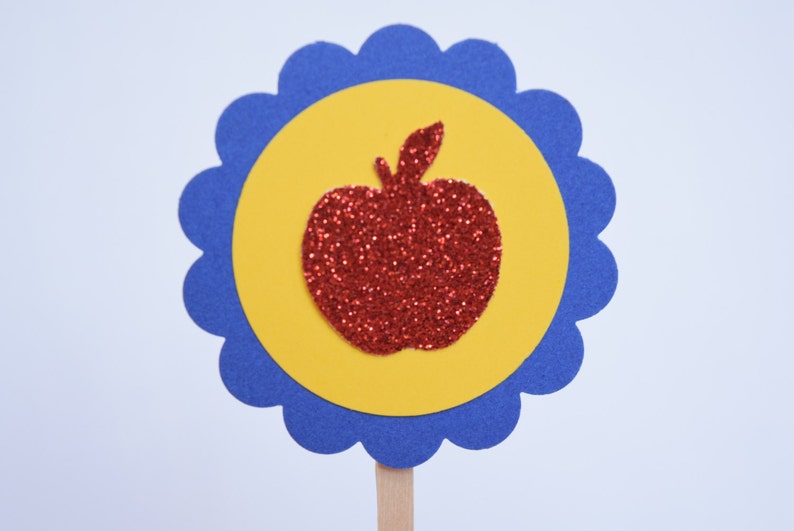 May include: A red glitter apple silhouette on a yellow circle with a blue scalloped border.