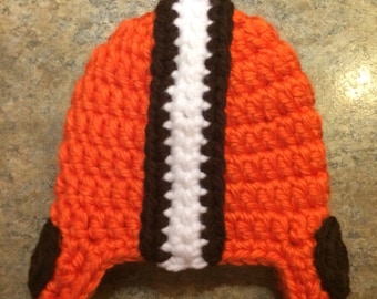 May include: Orange, brown, and white crocheted hat with ear flaps. The hat is shaped like a football helmet.