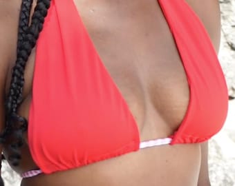 May include: A vibrant red halter bikini top. The top features a classic triangle design with a white and pink patterned trim. The fabric appears smooth and the style is suitable for swimwear.