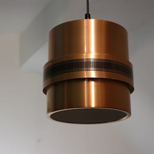 May include: A gold-toned pendant light with a black band around the middle. The light has a cylindrical shape and is made of metal.