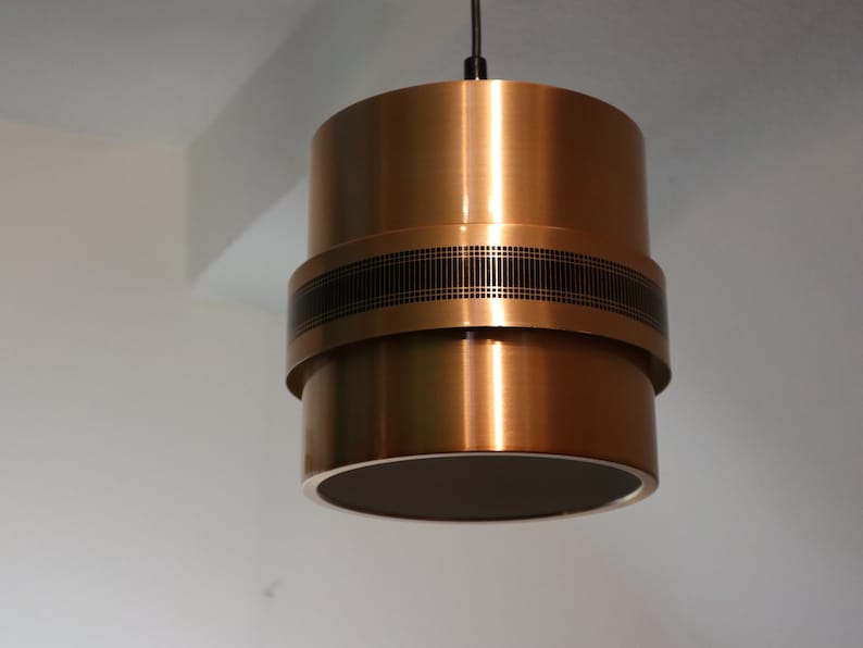 May include: A gold-toned pendant light with a black band around the middle. The light has a cylindrical shape and is made of metal.