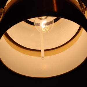 May include: A close-up of a light fixture with a white interior and a copper exterior. The light fixture has a single light bulb in the center.