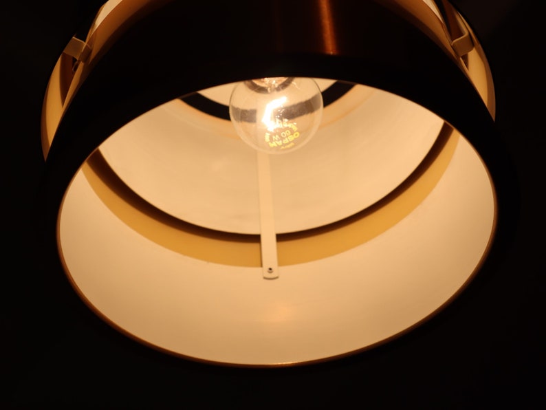 May include: A close-up of a light fixture with a white interior and a copper exterior. The light fixture has a single light bulb in the center.