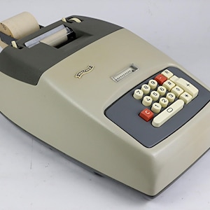 Puede incluir: Máquina de sumar Walther vintage en beige y gris. Cuenta con un teclado numérico con teclas rojas y blancas, un rollo de papel y el logotipo de Walther. Una máquina de oficina clásica.