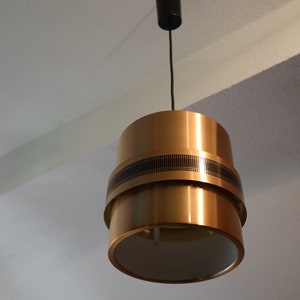 May include: A gold-toned pendant light with a black cord and a white inner shade. The light has a geometric design with a black band around the middle.