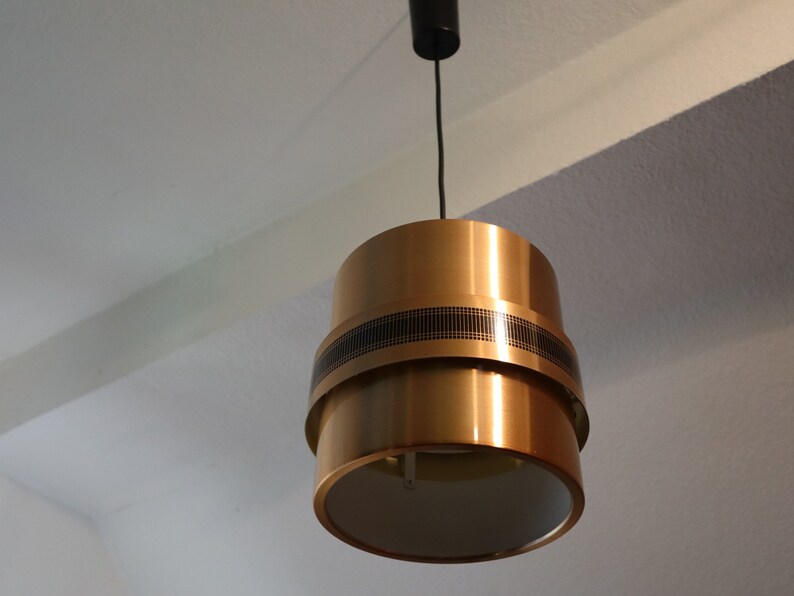 May include: A gold-toned pendant light with a black cord and a white inner shade. The light has a geometric design with a black band around the middle.