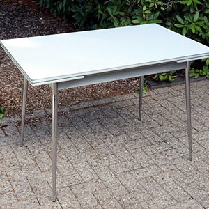 Op de afbeelding: Een rechthoekige tafel met een glad wit blad en vier slanke, zilverkleurige metalen poten. De tafel heeft een strak, vlak oppervlak en een eenvoudig frameontwerp, wat zorgt voor een stabiele constructie met een neutrale uitstraling.