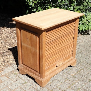 Könnte beinhalten: Ein hellbrauner Holzschrank mit Lamellenfront und Massivholzplatte. Der Schrank hat eine rechteckige Form und ist aus Naturholz gefertigt. Der Schrank steht auf einer Ziegeloberfläche.