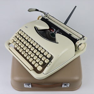 May include: A vintage white typewriter with a beige carrying case. The typewriter has a black ribbon and a beige keyboard with black lettering.