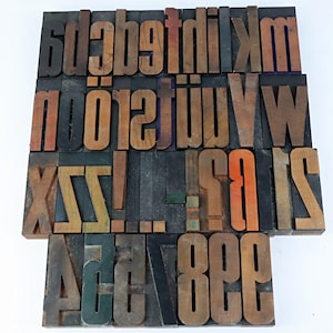 Puede incluir: Colección de bloques de impresión tipográfica de madera vintage. Los bloques presentan varias letras mayúsculas y minúsculas, números y signos de puntuación en una mezcla de fuentes y tamaños. Los bloques de madera son de varios tonos marrones.