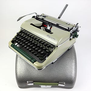 Peut inclure: Une machine à écrire vintage de couleur vert clair et argent, avec des touches noires et un levier de retour de chariot vert. La machine à écrire repose sur une mallette de transport grise avec une poignée verte. Le design est rétro et classique.