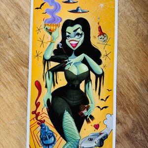 Puede incluir: Ilustración de una mujer de piel verde con un vestido negro, sosteniendo un cóctel y una muñeca. La obra presenta un fondo amarillo con murciélagos, una telaraña y un coche antiguo. La imagen tiene un tema retro y gótico.