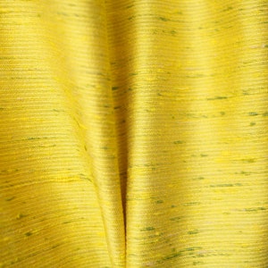 Może przedstawiać: Zbliżenie na żółtą tkaninę z subtelnym zielonym połyskiem. Tkanina ma splecioną strukturę i jest udrapowana w miękkie fałdy.