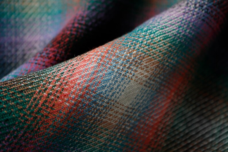 May include: Close-up of a woven fabric with a plaid pattern in shades of green, red, blue, and white.