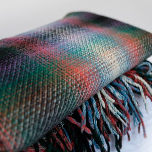 May include: A folded plaid throw blanket with a fringe border in shades of green, red, blue, and purple.