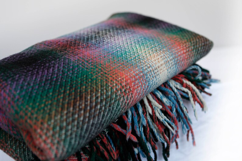 May include: A folded plaid throw blanket with a fringe border in shades of green, red, blue, and purple.