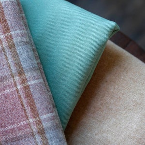 May include: Three fabric swatches in different textures and colors: a plaid pattern in brown and gray, a solid teal fabric, and a beige fabric with a subtle texture.
