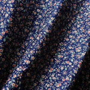 Pu&ograve; includere: Un tessuto blu navy con un piccolo motivo floreale bianco e rosa. Il tessuto &egrave; piegato e drappeggiato.