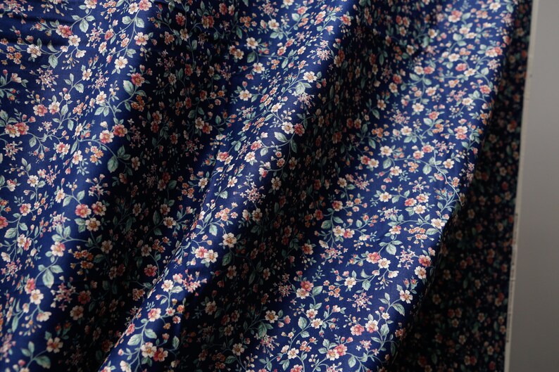 Pu&ograve; includere: Un tessuto blu navy con un piccolo motivo floreale bianco e rosa. Il tessuto &egrave; piegato e drappeggiato.