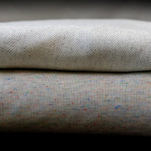 Może przedstawiać: Biały pled w jodełkę złożony na kolorowej poduszce ozdobnej.