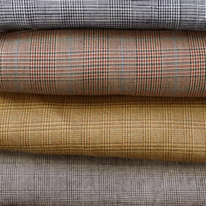 May include: A stack of folded fabric samples in various colors. The fabrics feature a classic plaid pattern in shades of navy, rust, gold, and gray. The close-up shot highlights the texture and detail of the woven material, suitable for apparel or home decor.