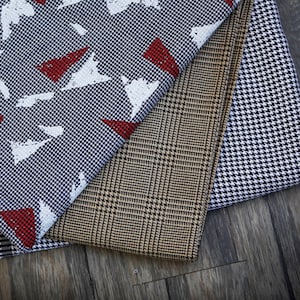 Op de afbeelding: Drie verschillende stofstalen met geometrische patronen. De bovenste staal is een blauwe en witte stof met rode driehoeken en witte verfspatten. De middelste staal is een bruine en beige stof met een ruitpatroon. De onderste staal is een zwarte en witte stof met een ruitpatroon.