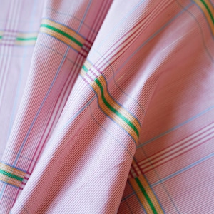 May include: Pink and white checkered fabric with thin green, yellow, and blue stripes. The fabric is folded and has a soft, textured appearance.