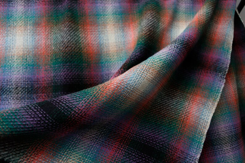 May include: Close-up of a soft, woven fabric with a plaid pattern in shades of red, green, purple, and white.