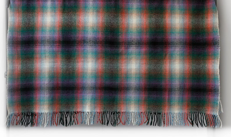 May include: A woven plaid throw blanket with a fringed edge in shades of black, red, green, blue, and white.