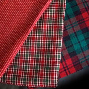 May include: Three fabric swatches in red, green, and white plaid patterns. The swatches are folded and layered on top of each other.